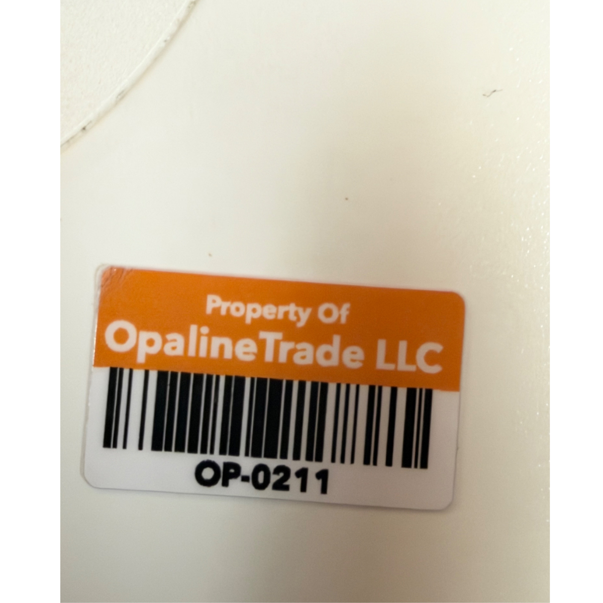 Close-up of an orange and white asset tag with a barcode that reads "Property Of OpalineTrade LLC" above the identification number OP-0211.