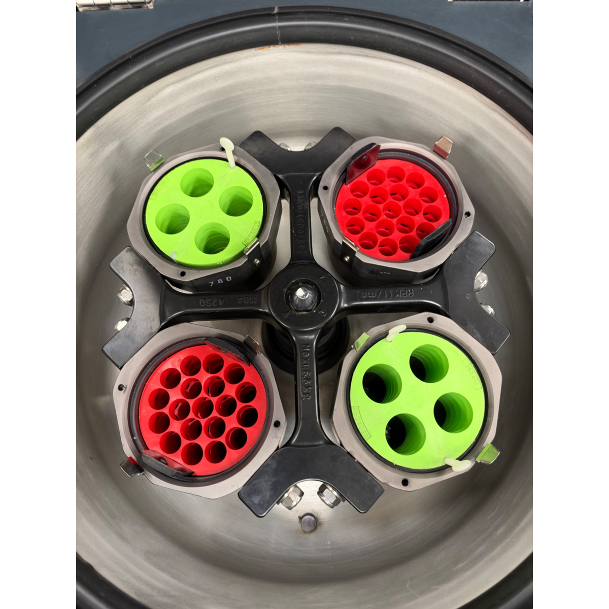 Top-down interior view of the centrifuge chamber showing the four-place swinging bucket rotor with two green and two red tube adapters.